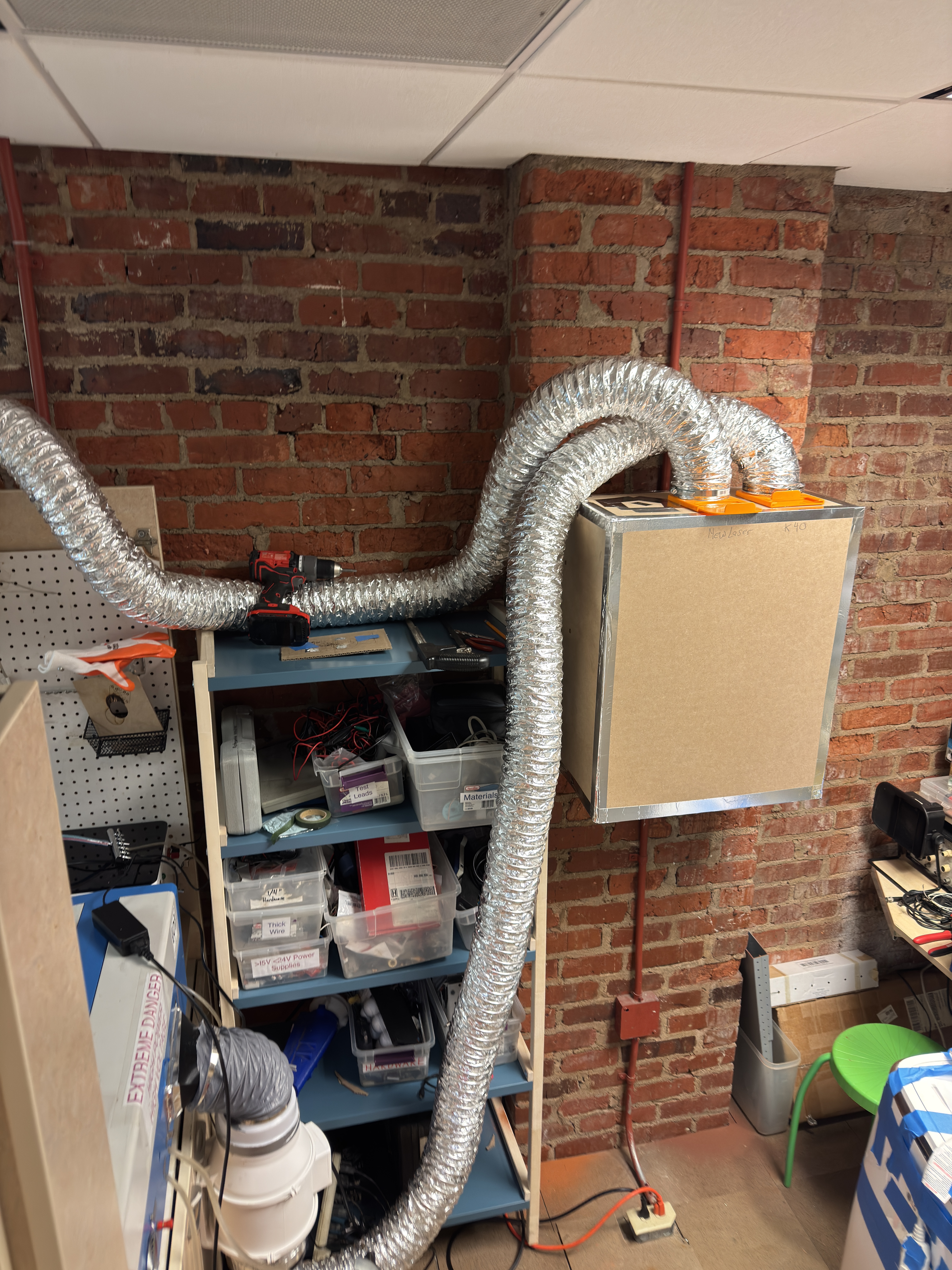 plain wooden box with aluminum-tape edges mounted on a brick wall with metal flex-ducts com,ing out of the top